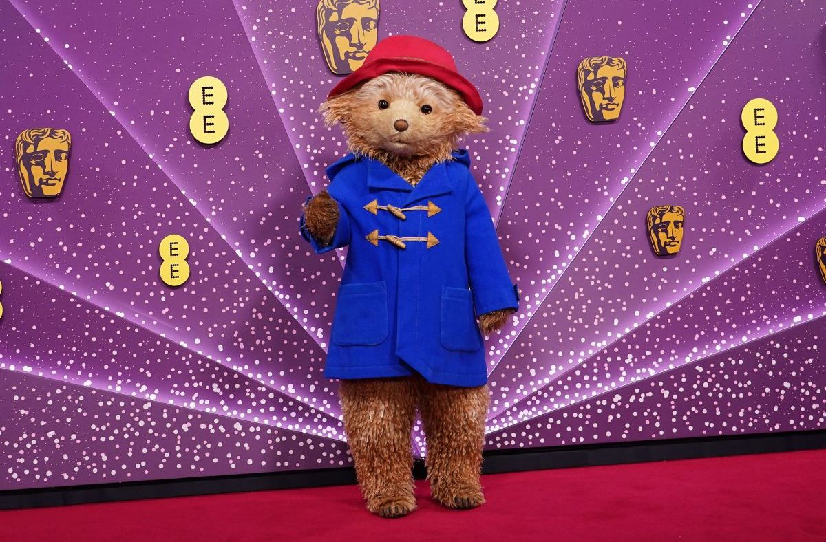 Paddington Bear in a blue duffle coat and red hat on a purple background with BAFTA and EE logos