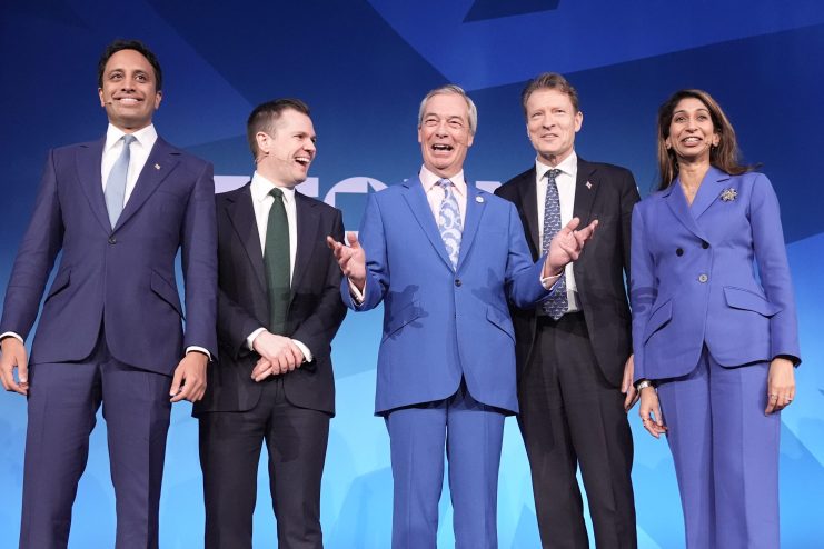 Reform UK leaders Nigel Farage, Richard Tice, and others smiling on stage against a blue background