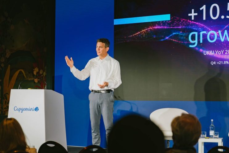 Rob Walker of Capgemini presenting on stage, with a digital screen showing +10.5 growth behind him.