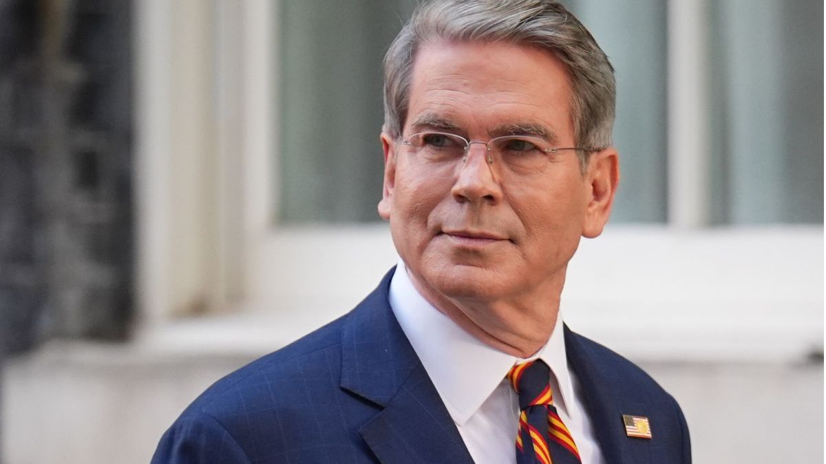 Scott Bessent, a man with gray hair and glasses, wearing a blue suit and striped tie, looking to the side.