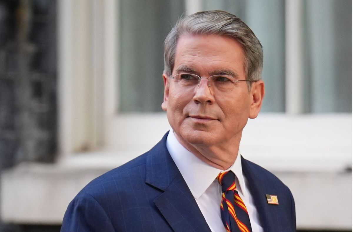 Scott Bessent, a man with gray hair and glasses, wearing a blue suit and striped tie, looking to the side.