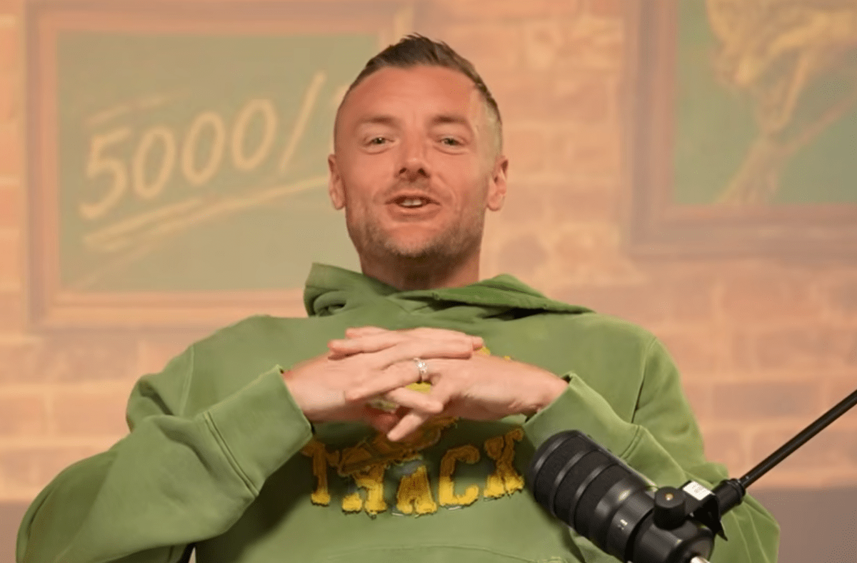 Man in a green hoodie speaking into a microphone, with a 5000 sign in the background.