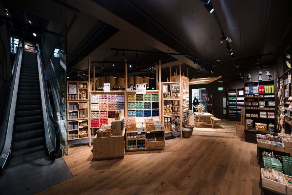 Interior of a Sostrene Grene store with wooden shelves, colorful yarn, craft supplies, and an escalator.