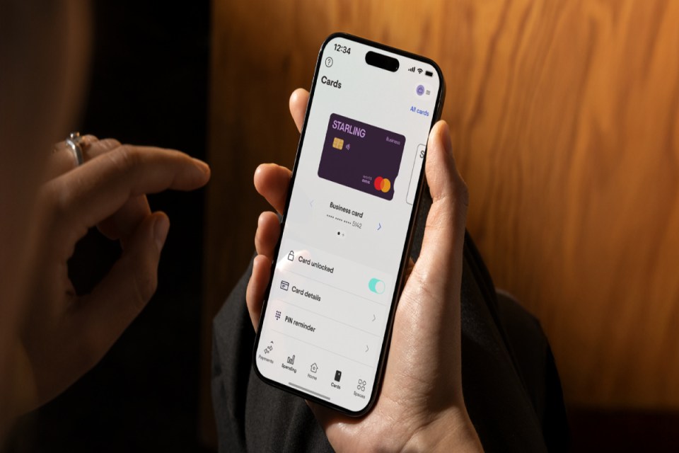 Hand holding iPhone displaying Starling CardHub Business app with virtual debit card and options