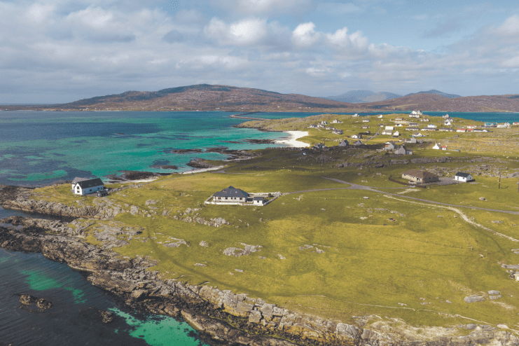Aerial view of Outer Hebrides coastline, turquoise sea, white sand beach, green fields, and scattered homes.