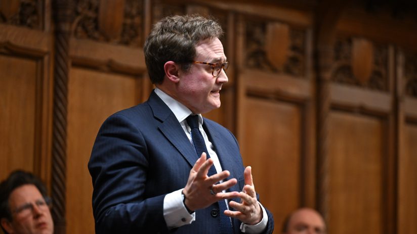 Tom Tugendhat, MP, speaks passionately, gesturing with hands in a formal setting with wood paneling.