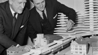 Two town planners examining a London monorail concept model with buildings and a proposed elevated train line.