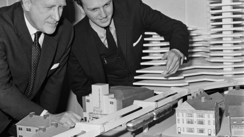 Two town planners examining a London monorail concept model with buildings and a proposed elevated train line.