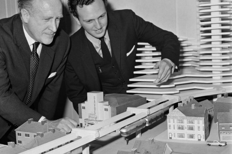 Two town planners examining a London monorail concept model with buildings and a proposed elevated train line.