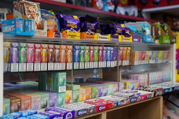 Retail display shelf in a shop showing various vape products, candy, and gum, with clear pricing and warning labels.