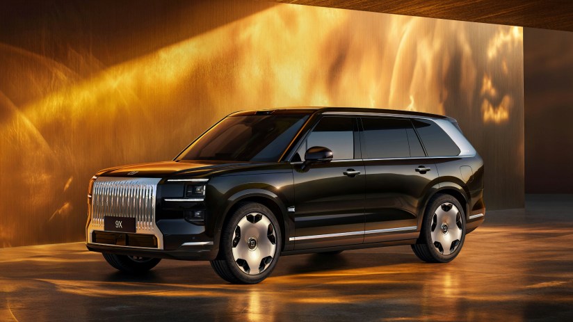 Dark brown Zeekr X9 electric MPV with large chrome grille, parked indoors with warm golden lighting.
