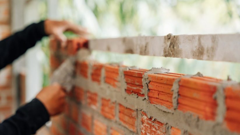 Construction workers hands building a brick wall with mortar and a leveling tool, demonstrating masonry work