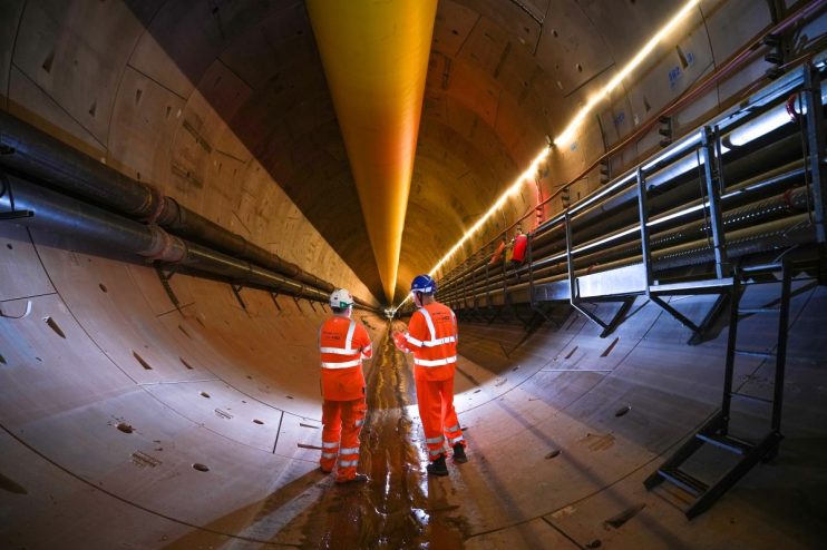 Two engineers in hard hats and high-visibility gear inspecting a large, illuminated tunnel under construction.
