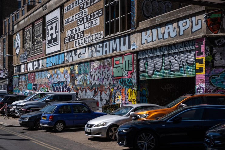 Vibrant graffiti art covering a brick building with parked cars in front, Truman Brewery area.