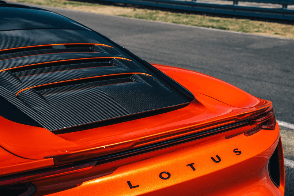 Rear view of an orange Lotus sports car with carbon fiber engine cover on a racetrack
