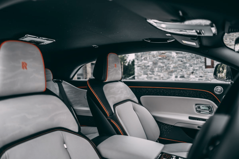 Luxurious car interior with custom light grey and black seats, orange piping, and illuminated door panel details