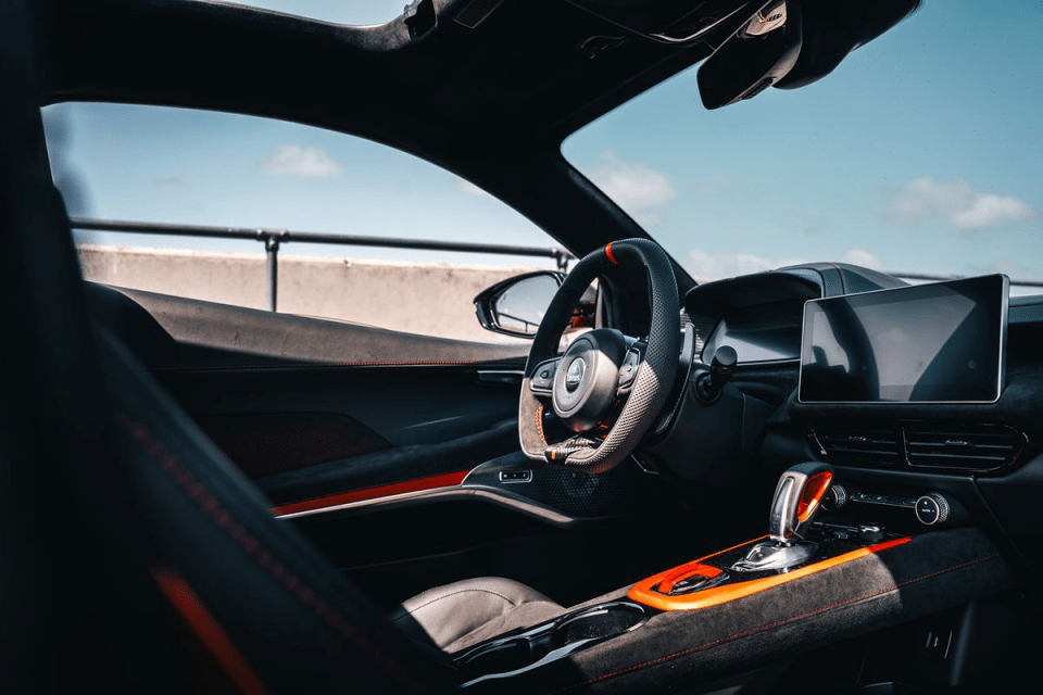 Modern car interior with black leather, orange accents, steering wheel, digital display, and gear selector.