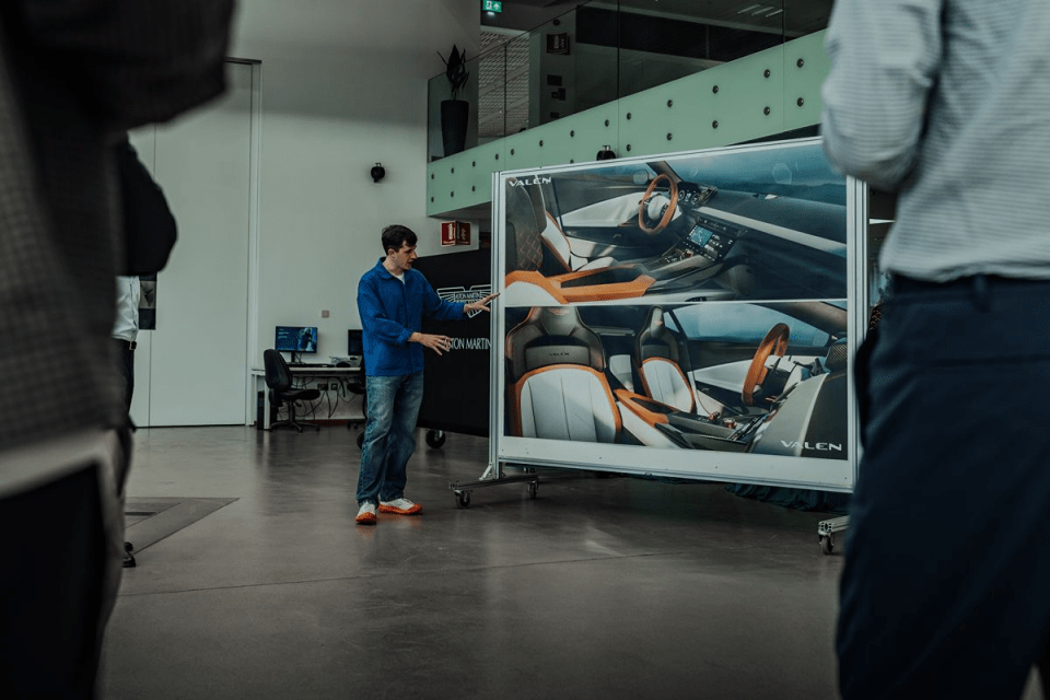 Man in blue shirt presenting car interior designs on a large display board in a modern office.