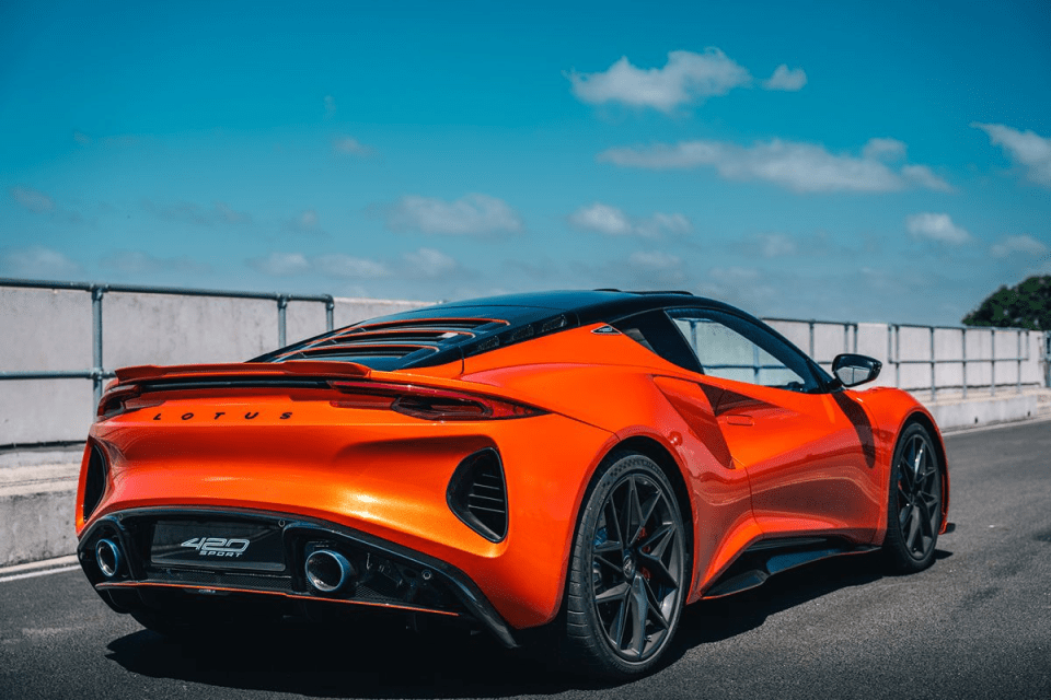 Rear view of an orange Lotus Emira 420 Sport on a race track under a blue sky