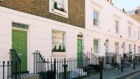 Row of classic London terraced houses with white facades and green doors, indicating UK property.