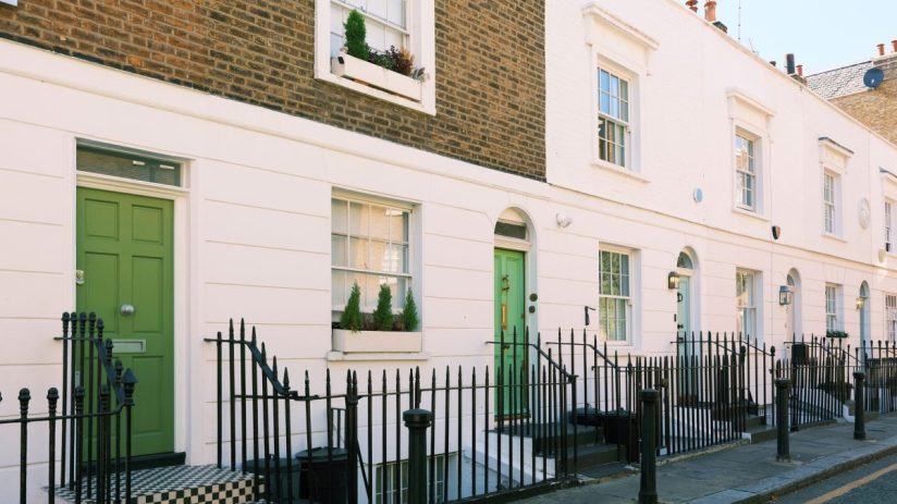 Row of classic London terraced houses with white facades and green doors, indicating UK property.