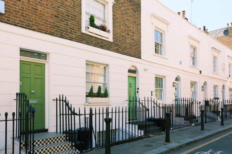 Row of classic London terraced houses with white facades and green doors, indicating UK property.
