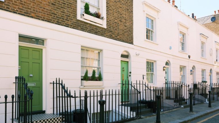 Row of classic London terraced houses with white facades and green doors, indicating UK property.
