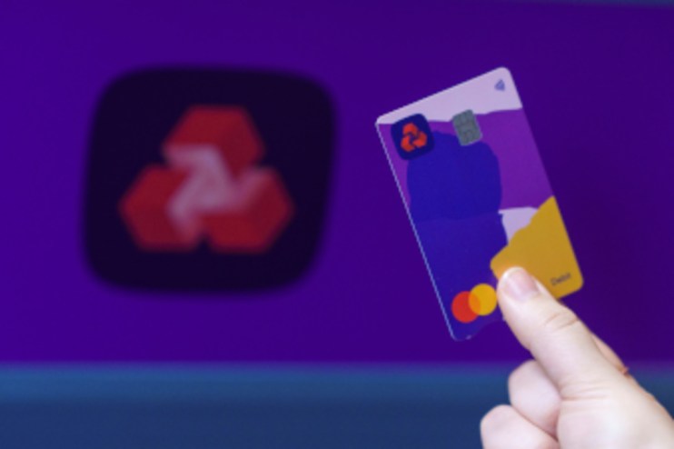 Hand holding a NatWest debit card with a colorful design, blurred NatWest logo in the background.