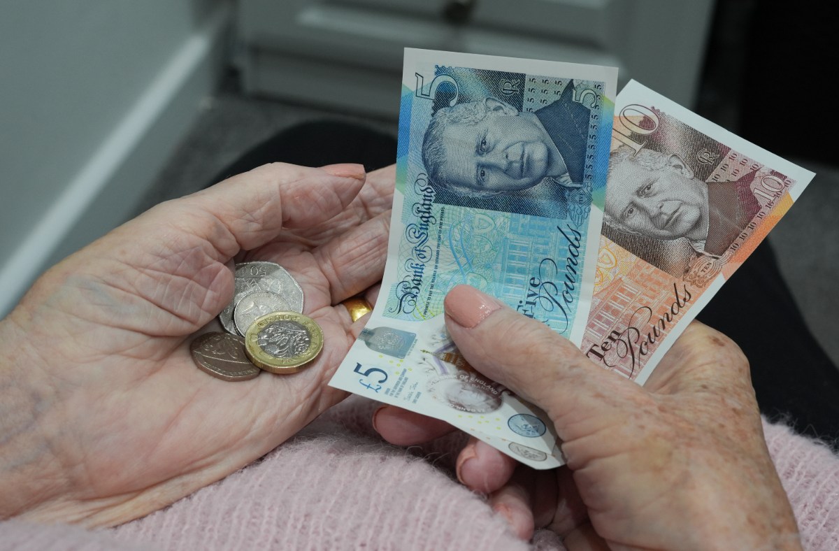 Elderly hands holding British pound notes (£5, £10) and coins, representing pension funds and finances.