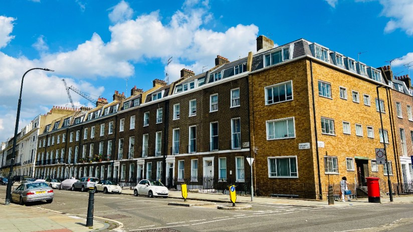 Street scene with historic London row houses, parked cars, crosswalk, and a red mailbox under a blue sky