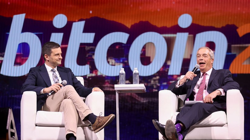 Nigel Farage and another man on stage discussing crypto and UK reform, with Bitcoin on screen.