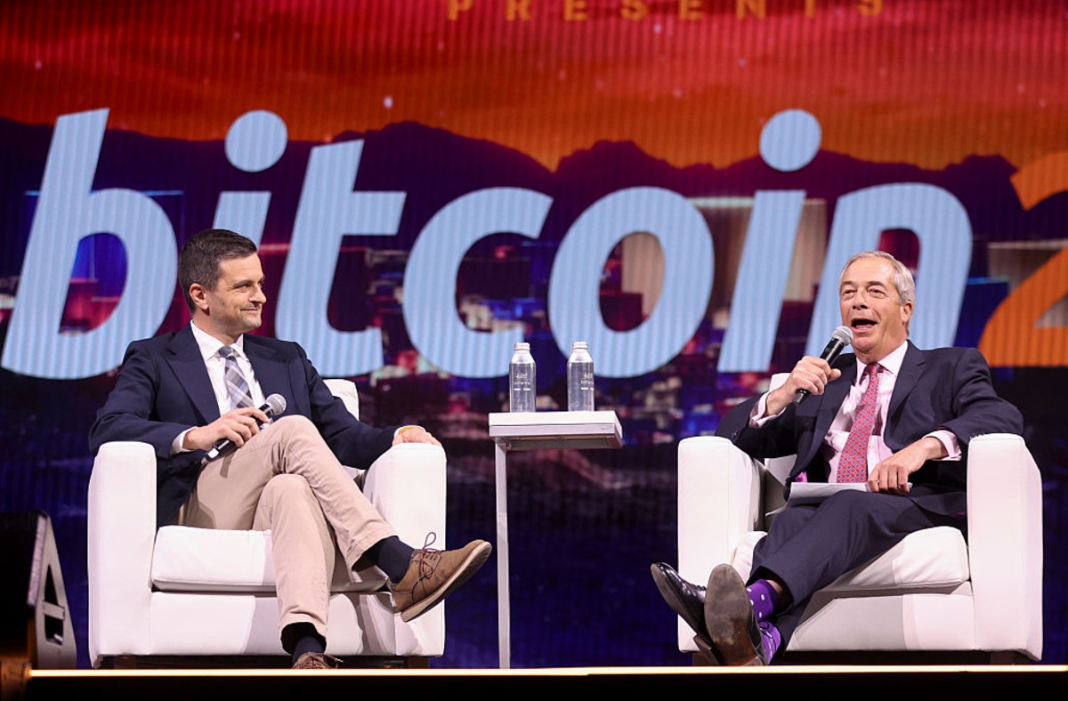 Nigel Farage and another man on stage discussing crypto and UK reform, with Bitcoin on screen.
