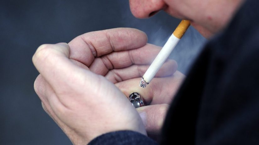 Close-up of a person lighting a cigarette with a silver lighter, smoke rising from the tip.