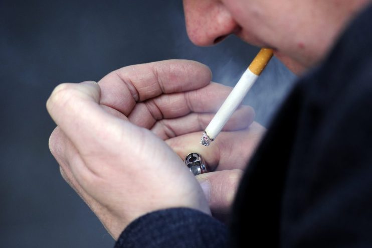 Close-up of a person lighting a cigarette with a silver lighter, smoke rising from the tip.