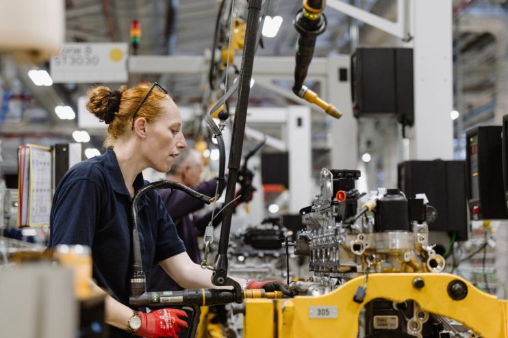 Female factory worker in red gloves assembling machinery on an industrial production line.