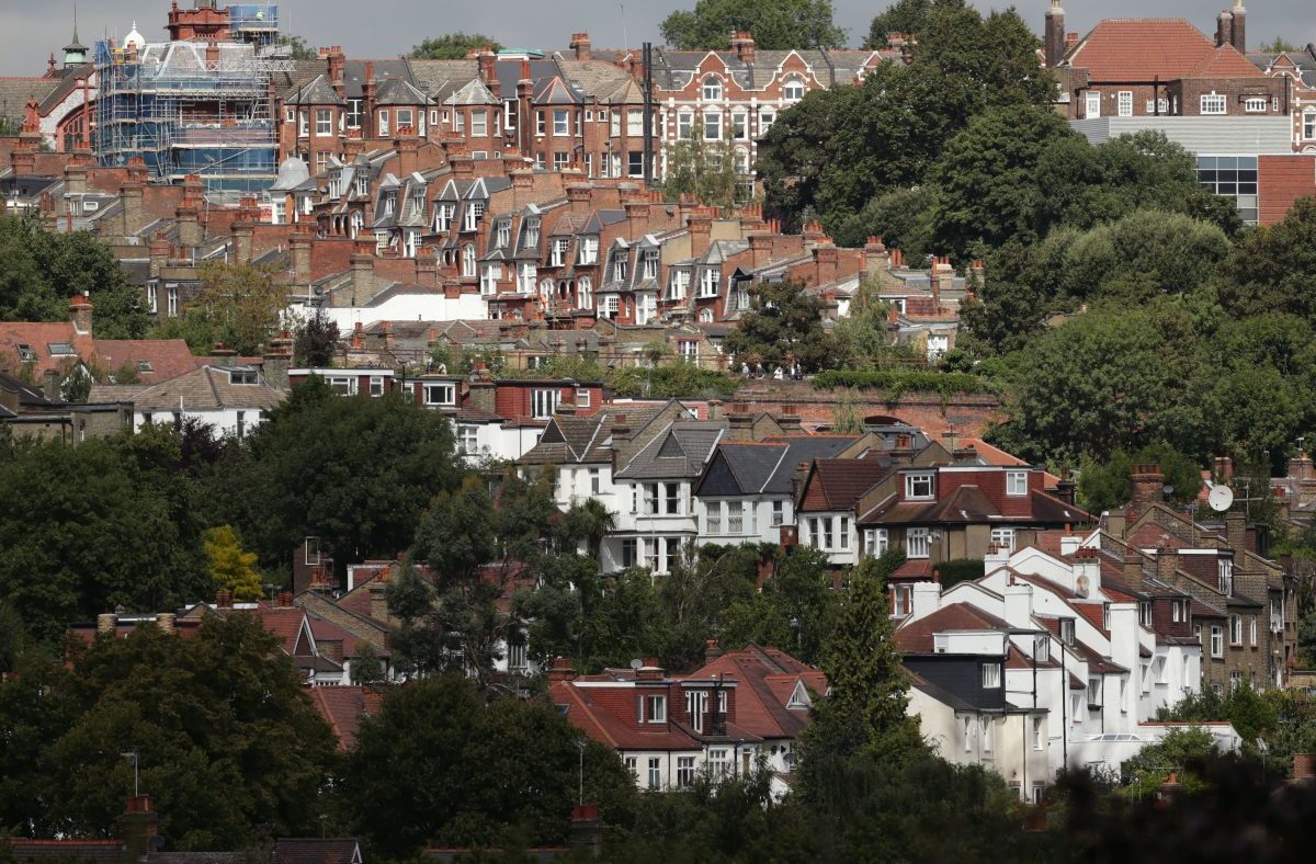 Dense housing on a hillside with traditional brick and white stucco homes, some under construction, surrounded by trees.