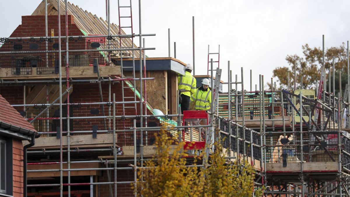 Construction workers in hard hats and high-visibility jackets on scaffolding at a new build house site