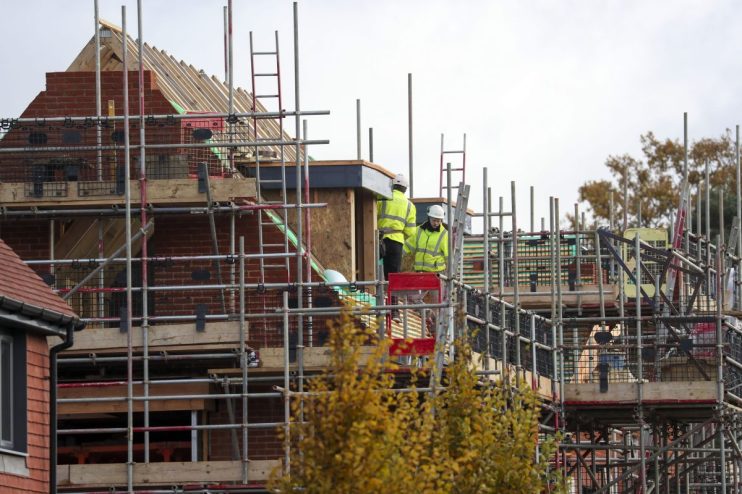 Construction workers in hard hats and high-visibility jackets on scaffolding at a new build housing development.