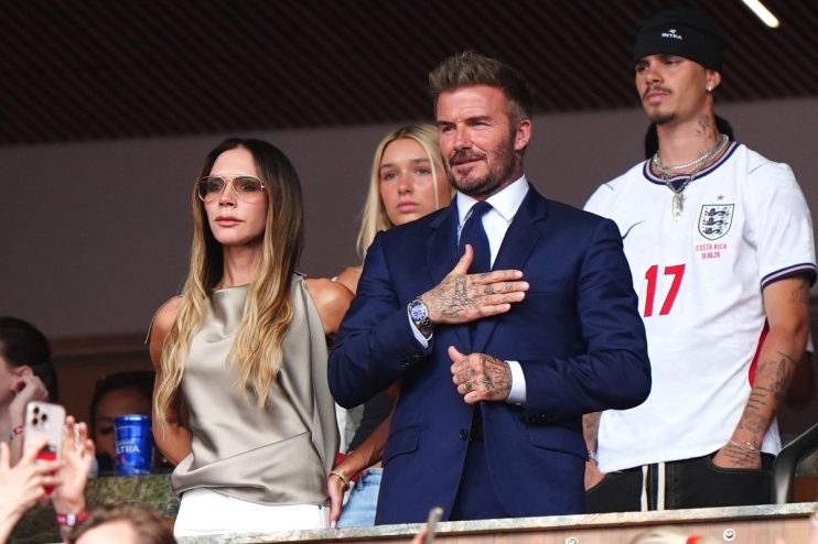 David Beckham in a navy suit with hand on chest, Victoria Beckham in sunglasses, and Brooklyn Beckham in an England jersey.