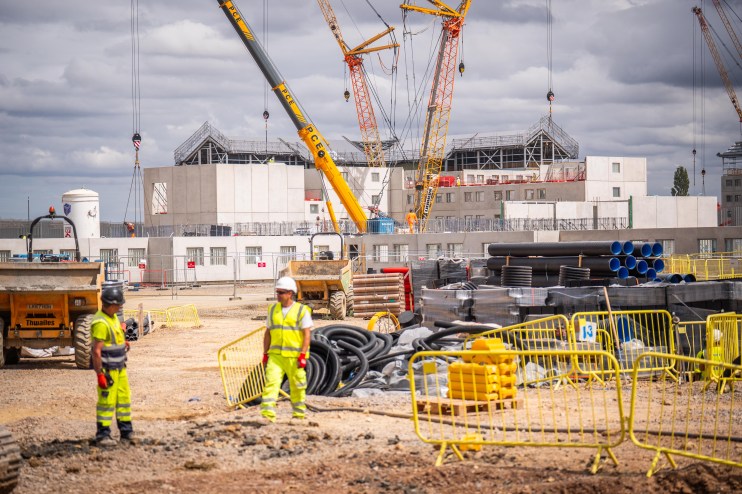 Construction site with two workers, cranes, building materials, and a building under construction.