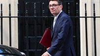 Andy Burnham, Mayor of Greater Manchester, in a suit, holding a red folder, walking past railings