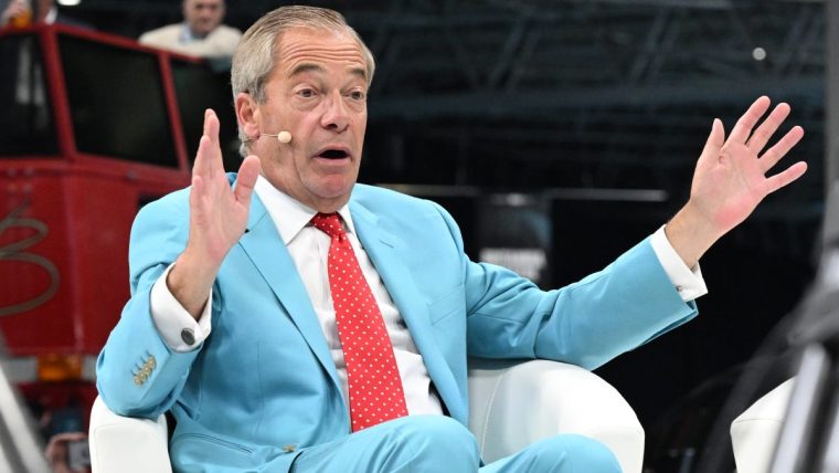 Nigel Farage in a light blue suit and red polka dot tie, speaking with hands raised, at a public event.