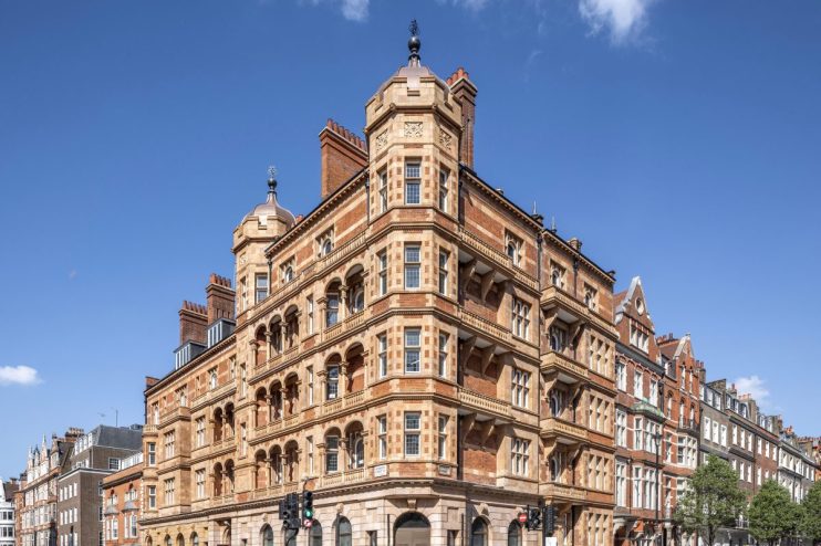 Ornate red brick and stone building at 1 Harley Street in London, with pedestrians crossing the street on a sunny day.