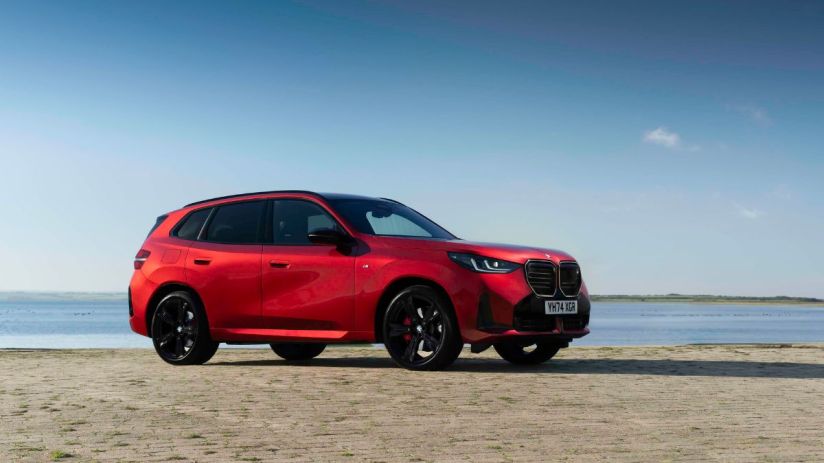 Red BMW X3 SUV parked on a paved surface next to calm water under a clear blue sky