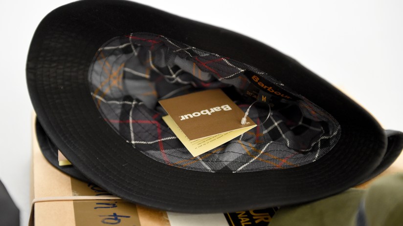 Barbour black hat with tartan lining and product tags, showcasing classic British family business apparel