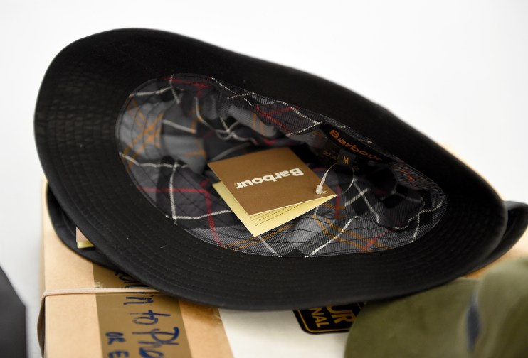 Barbour black hat with tartan lining and product tags, showcasing classic British family business apparel