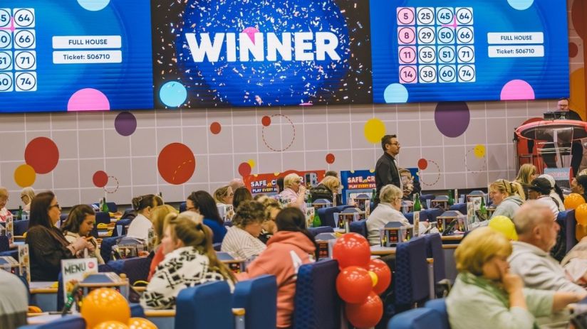Buzz Bingo hall with players, a large screen displaying WINNER and FULL HOUSE for ticket 506710