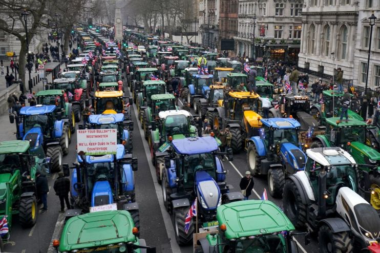 Long line of tractors, many with Union Jack flags, protesting in a city street, one sign reads Keep your bullsh*t in Westm...