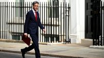 Ed Miliband in a suit and red tie, carrying a red folder, walking past railings outside Downing Street