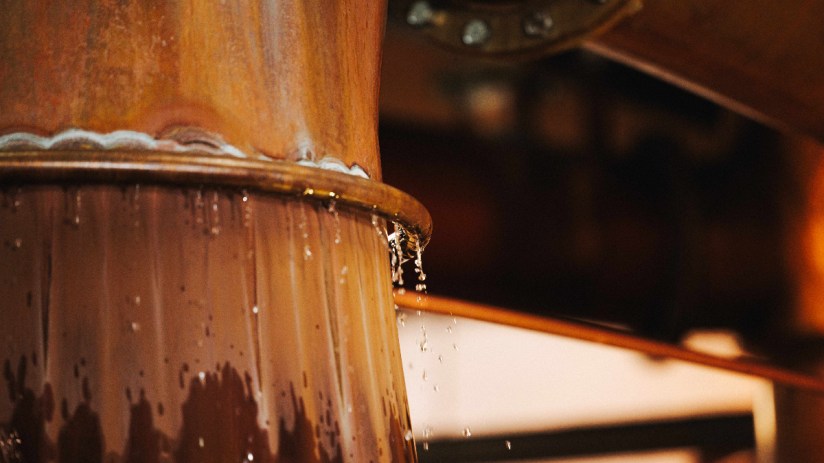 Close-up of water dripping from the copper cooling ring of a Fettercairn whisky still.
